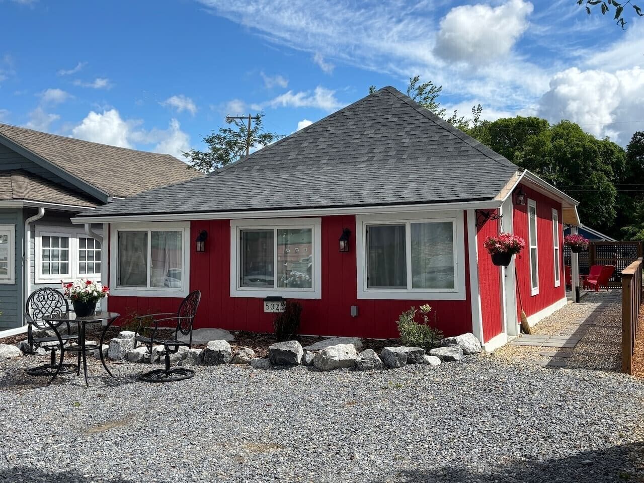 Une maison rouge avec une allée en gravier et un patio comprenant une table et des chaises.