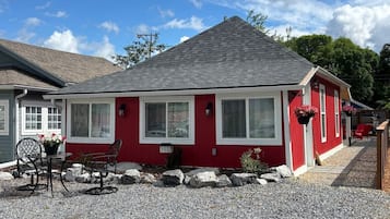 Une maison rouge avec une allée en gravier et un patio comprenant une table et des chaises.