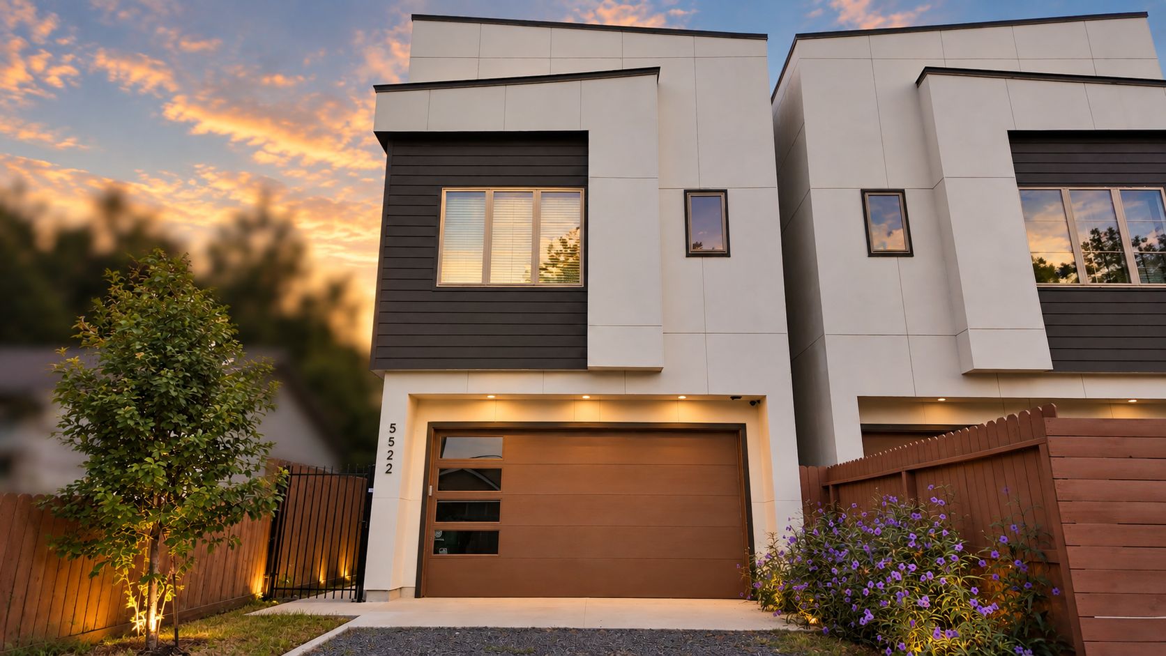 A modern two-story house with a garage, a small tree, and a wooden fence.