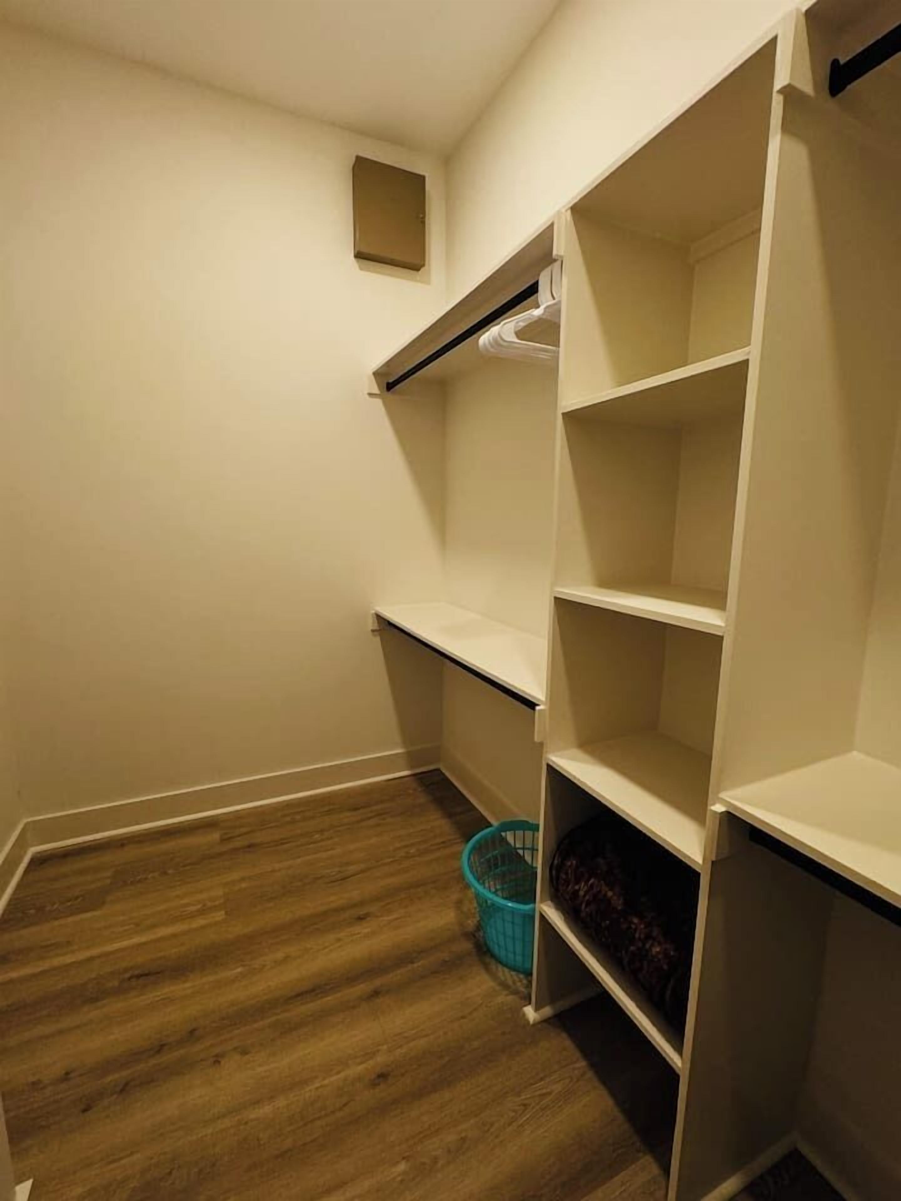 A closet with open shelves and a blue basket on the floor.
