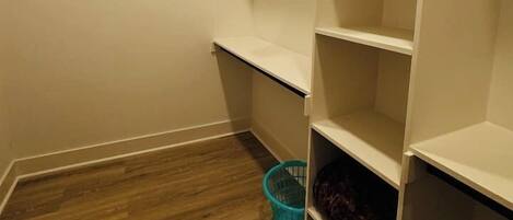 A closet with open shelves and a blue basket on the floor.