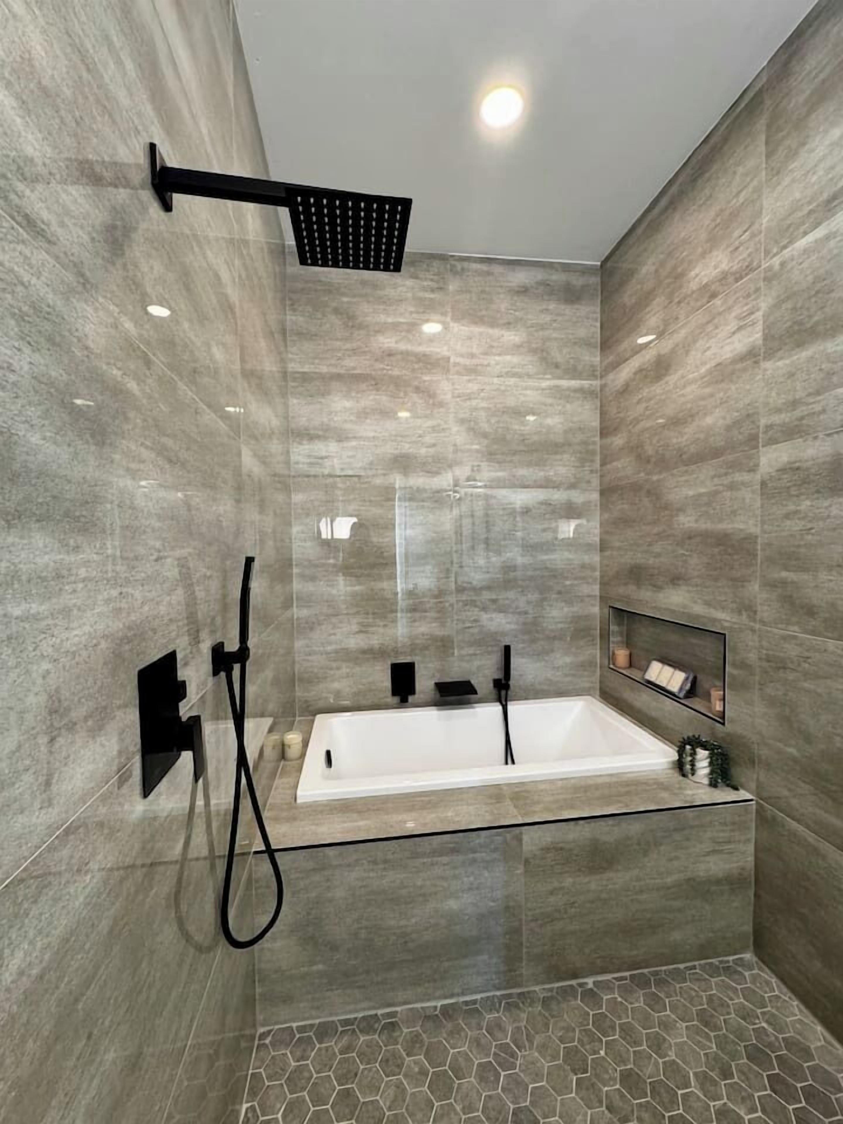A modern bathroom with a glass-enclosed bathtub, a handheld showerhead, and a built-in shelf.