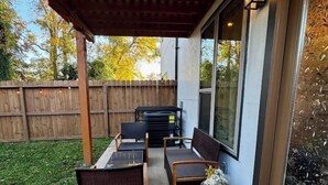 Un patio techado con mobiliario exterior, un jarrón decorativo y una valla de madera al fondo.