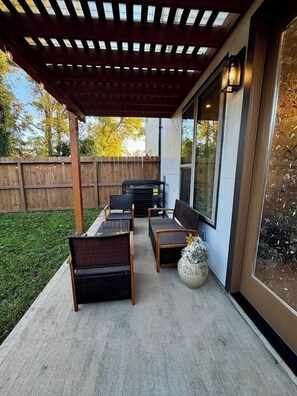 Eine überdachte Terrasse mit Gartenmöbeln, einer dekorativen Vase und einem Holzzaun im Hintergrund.