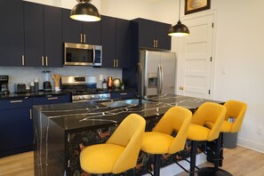 Cozinha moderna com armários azul escuro, bancada de mármore preto e banquetas amarelas.