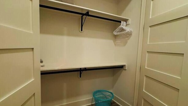 Un armario con puertas abiertas, suelo de madera y una cesta azul.