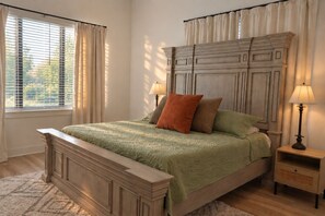 Ein Schlafzimmer mit einem großen Bett, einem Nachttisch, einer Lampe und einem Fenster mit Vorhängen.
