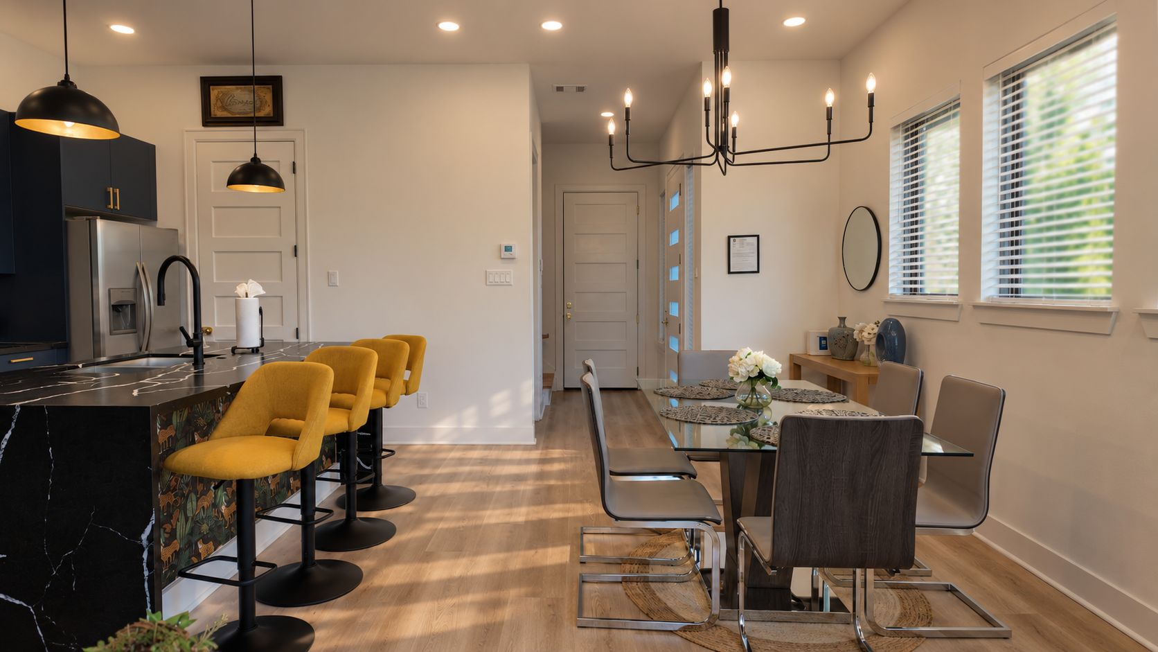 Une cuisine moderne avec un plan de travail en marbre noir, des tabourets de bar jaunes et un coin repas comprenant une table et des chaises en verre.