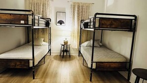 Una habitación con dos literas, un ventilador de techo, una mesita pequeña y una ventana con cortinas.