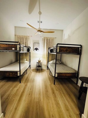 Ein Zimmer mit zwei Etagenbetten, einem Deckenventilator, einem kleinen Tisch und einem Fenster mit Vorhängen.