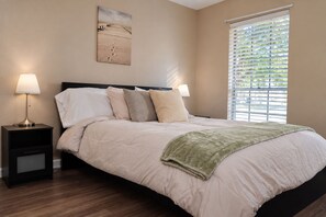 A bedroom with a bed, two bedside tables, a lamp, a window with blinds, and a wall-mounted artwork. - Houston 2BR Stay | Near NRG, & Downtown | Coffee (Houston)