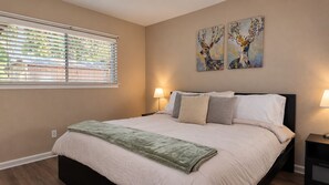A bedroom with a bed, two bedside lamps, a window with blinds, and two wall-mounted paintings. - Houston 2BR Stay | Near NRG, & Downtown | Coffee (Houston)