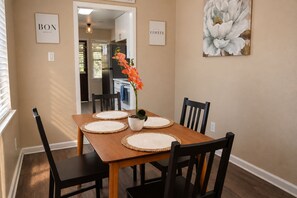 A dining area with a wooden table, four chairs, and a vase with flowers. There are two framed signs on the wall, one reading 'BON APPETIT' and the other 'COFFEE'. - Houston 2BR Stay | Near NRG, & Downtown | Coffee (Houston)