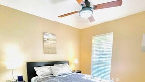 Ein Schlafzimmer mit einem Bett, Nachttischen, einem Deckenventilator und einem Fenster.