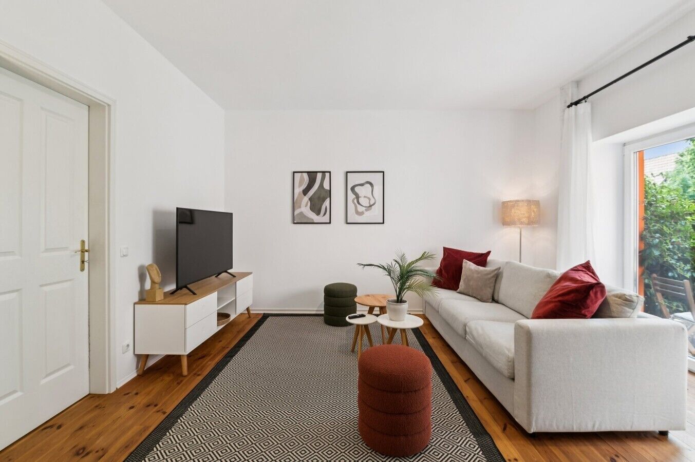 Ein stilvolles Wohnzimmer mit einer Couch, einem Fernseher, einem kleinen Tisch mit Pflanze und einem Teppich.