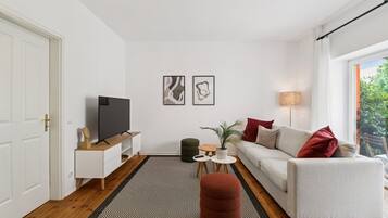 Ein stilvolles Wohnzimmer mit einer Couch, einem Fernseher, einem kleinen Tisch mit Pflanze und einem Teppich.