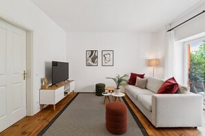 Ein stilvolles Wohnzimmer mit einer Couch, einem Fernseher, einem kleinen Tisch mit Pflanze und einem Teppich.