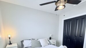Ein Schlafzimmer mit einem Bett, einem Nachttisch, einem Deckenventilator und einer Tür.