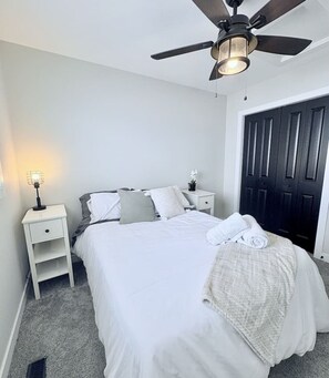 Ein Schlafzimmer mit einem Bett, einem Nachttisch, einem Deckenventilator und einer Tür.