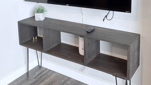 Ein Flachbildfernseher an einer Wand, über einem dunklen Holzschrank mit Regalen.