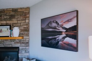 Ein Zimmer mit Kamin, Steinwand, gerahmtem Bild, weißer Vase und großem Landschaftsbild.
