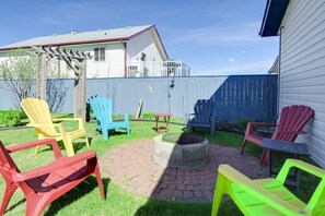 En baghave med et bålsted, flere Adirondack-stole og en træpergola.