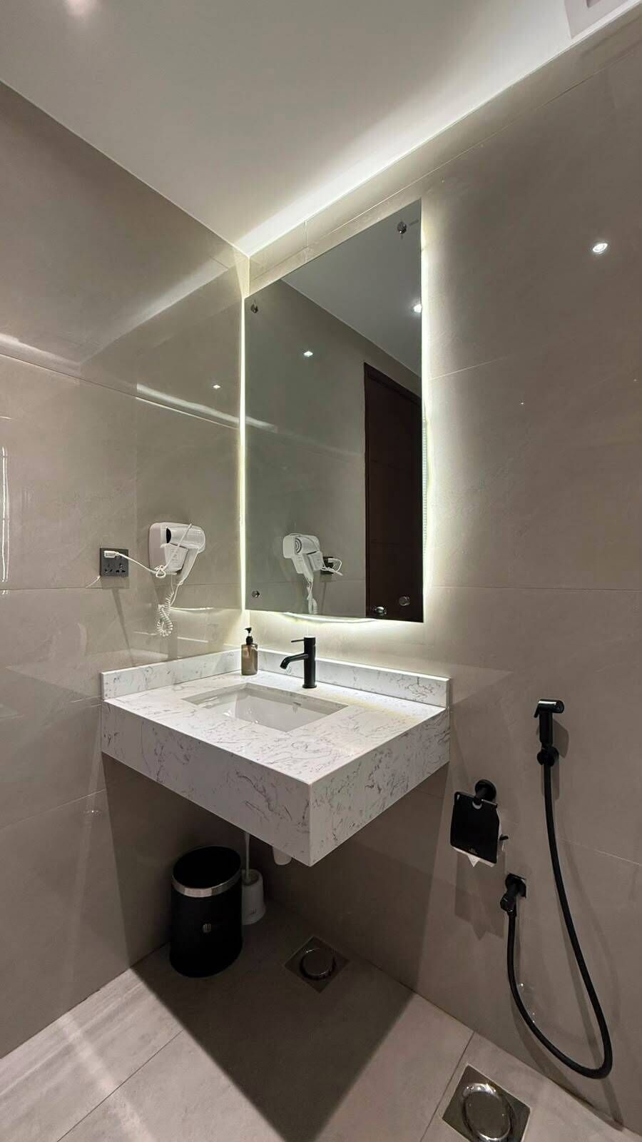 Une salle de bain moderne avec un lavabo en marbre, un grand miroir et une douchette à main.