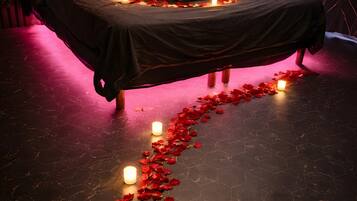 Un lit recouvert de pétales de rose et décoré de bougies, une tête de lit en bois et un plancher sombre.