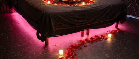 A bed with rose petals and candles, a wooden headboard, and a dark floor.