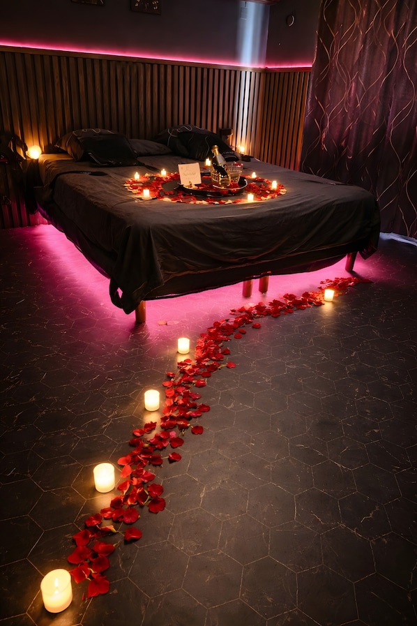 A bed with rose petals and candles, a wooden headboard, and a dark floor.