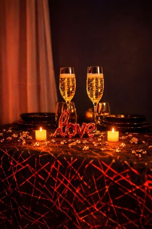 Et bord dækket med to champagneglas, et tændt stearinlys og et dekorativt skilt med ordet 'love'.
