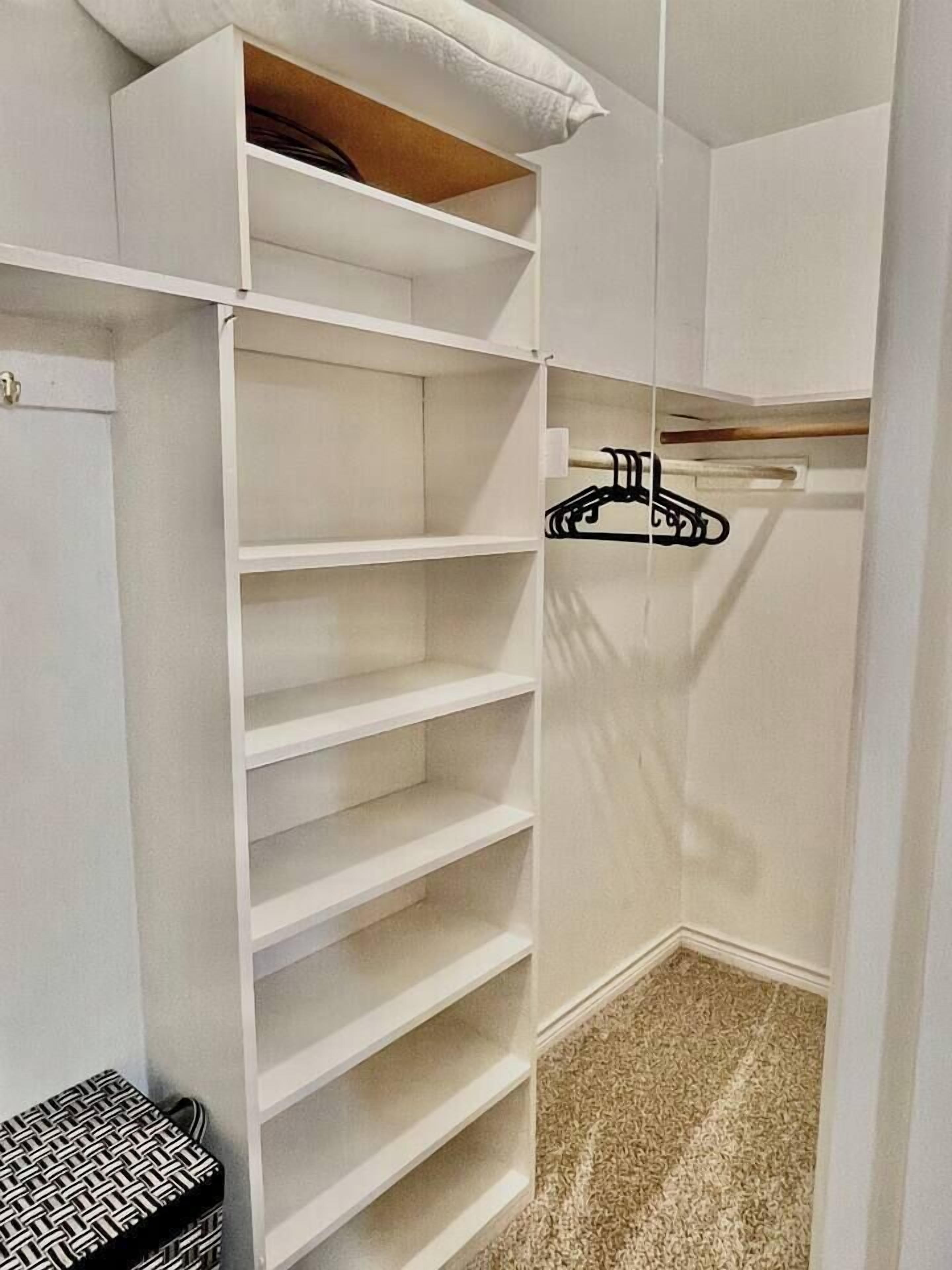 En vit garderob med flera hyllor och en klädstång.
