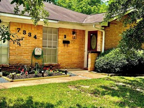 A brick house with a number '7334' on the wall, a front door, and a small garden area. - Spring Branch 2BR Private Patio + Workspace (Houston)