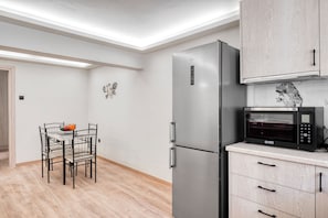 A modern kitchen with a stainless steel refrigerator, a microwave, and wooden cabinets. - Charming 1-Bedroom Garden Apartment Near Glyfada Center & Beach (Glyfada)