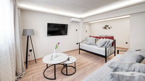 Ein modernes Wohnzimmer mit einer Couch, einem kleinen runden Tisch, einem Fernseher und einer Klimaanlage.