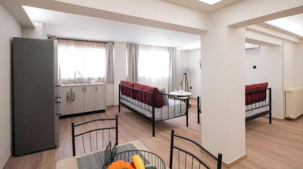 A compact living space with a kitchenette, two single beds, a dining table, and a small window.