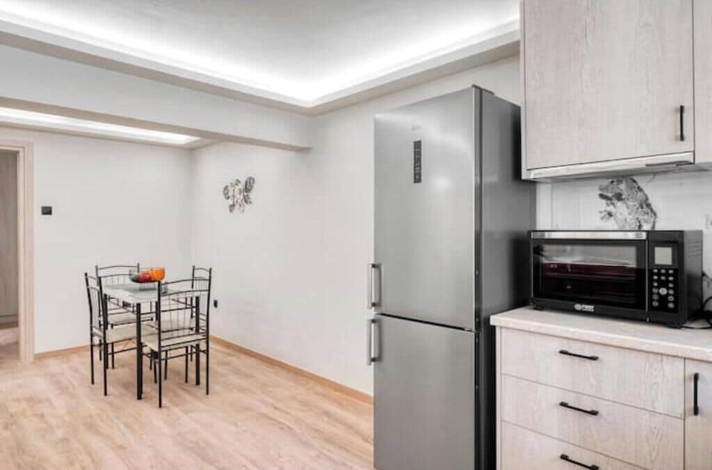 A modern kitchen with a stainless steel refrigerator, a microwave, and a dining area with a metal chair and table.