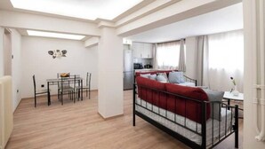 Ein kompakter Wohnbereich mit Essplatz, einem Bett mit roter Bettwäsche und einer kleinen Küchenzeile im Hintergrund.