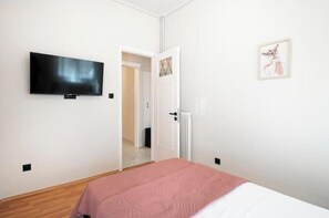 Ein Schlafzimmer mit einem Bett, einem Fernseher, einer Tür und einem gerahmten Bild an der Wand.