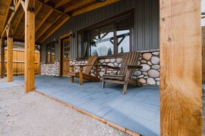 Ein überdachter Außenbereich mit Holzstühlen, einer Steinwand und einer Holzhütte mit geneigtem Dach.