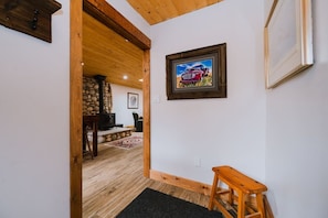 A hallway with a wooden bench, a framed picture on the wall, and a stone fireplace in the background. - The Old West Cabin Steps from the Lake (Sylvan Lake)