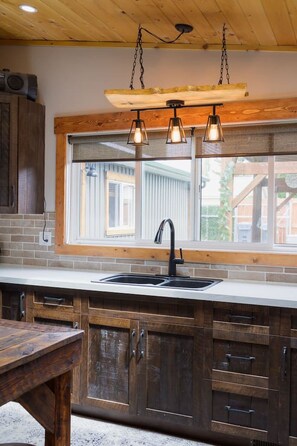 Une cuisine dotée d’une grande fenêtre, de meubles en bois, d’un robinet noir et de luminaires suspendus.