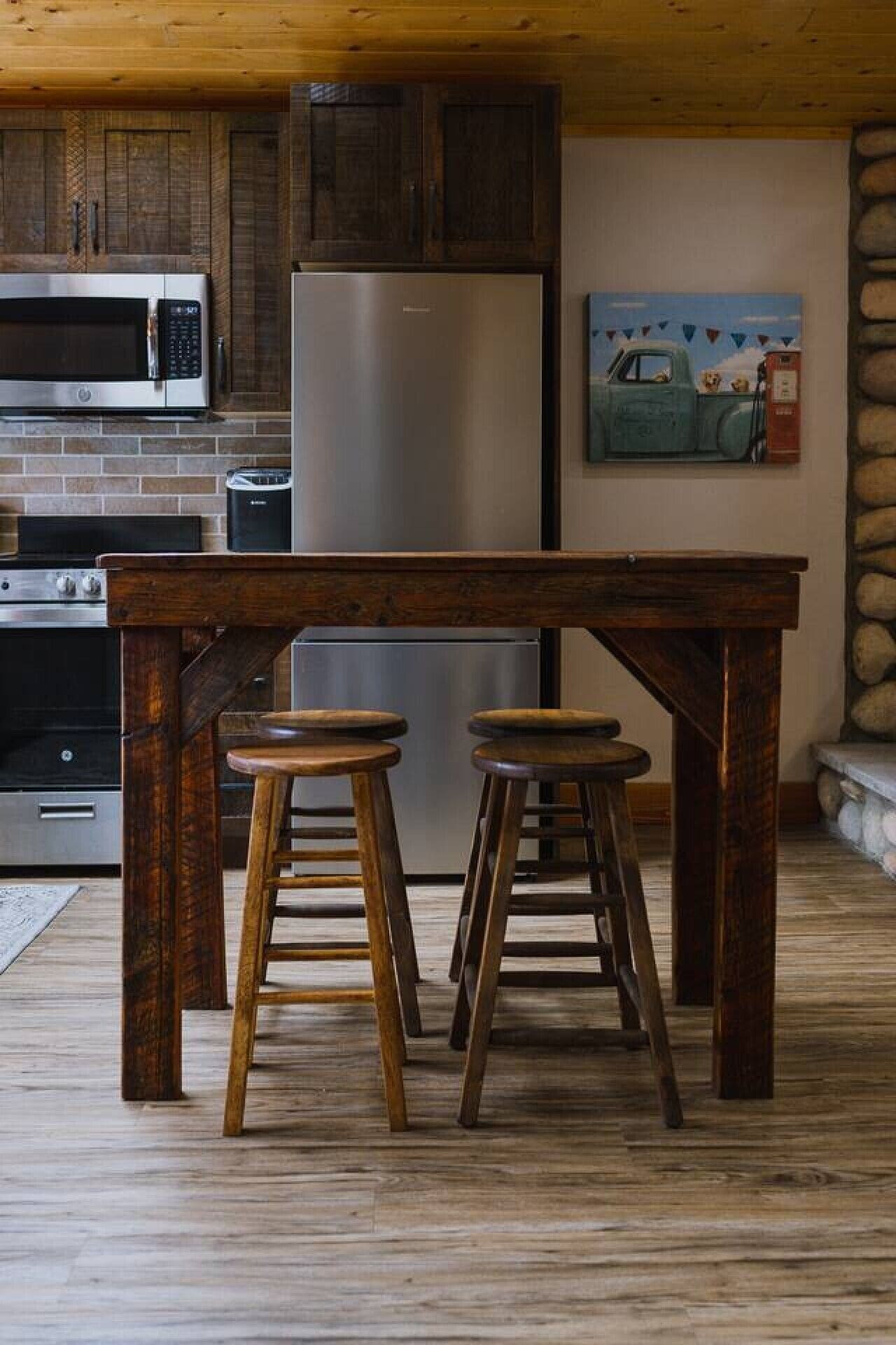 A kitchen with a wooden table and stools, a refrigerator, a microwave, and a painting on the wall.