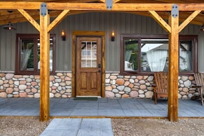 Une véranda en bois avec un mur en pierre, une porte en bois et deux fenêtres avec des rideaux.