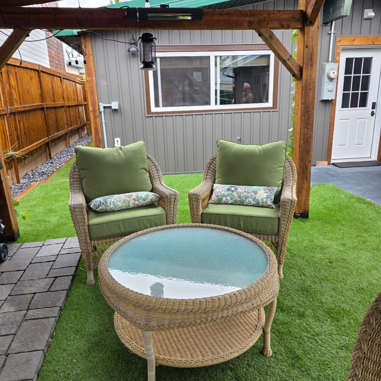 En overdækket terrasse med fletningsmøbler og kunstgræs.