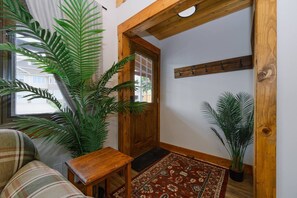 A cozy entryway with a wooden door, a small table, a patterned rug, and large green plants.