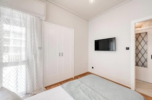 Ein Schlafzimmer mit einem Bett, einem Kleiderschrank, einem Fernseher und einem Fenster mit Vorhängen.