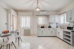 A modern kitchen with white cabinetry, a dining table with chairs, and a built-in oven. - Spacious 2-Bedroom Apartment with Balcony Near Glyfada Center & Beach (Glyfada)