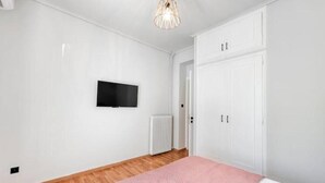 Et soveværelse med en seng, et tv monteret på væggen, en radiator og et skab.