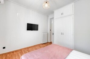 A bedroom with a bed, a television mounted on the wall, a radiator, and a wardrobe. - Spacious 2-Bedroom Apartment with Balcony Near Glyfada Center & Beach (Glyfada)